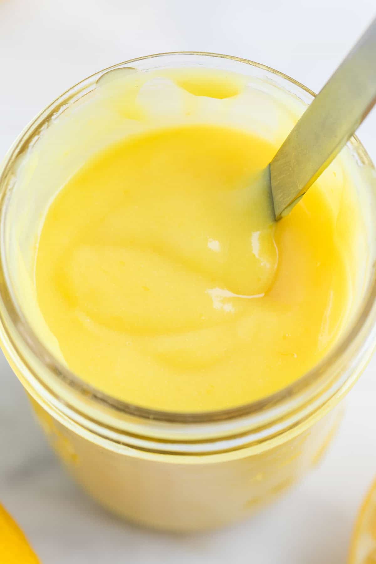 Jar of vegan lemon curd with a spoon inside.