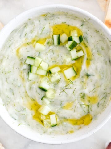 Bowl of vegan tzatziki sauce garnished with cucumber and olive oil.
