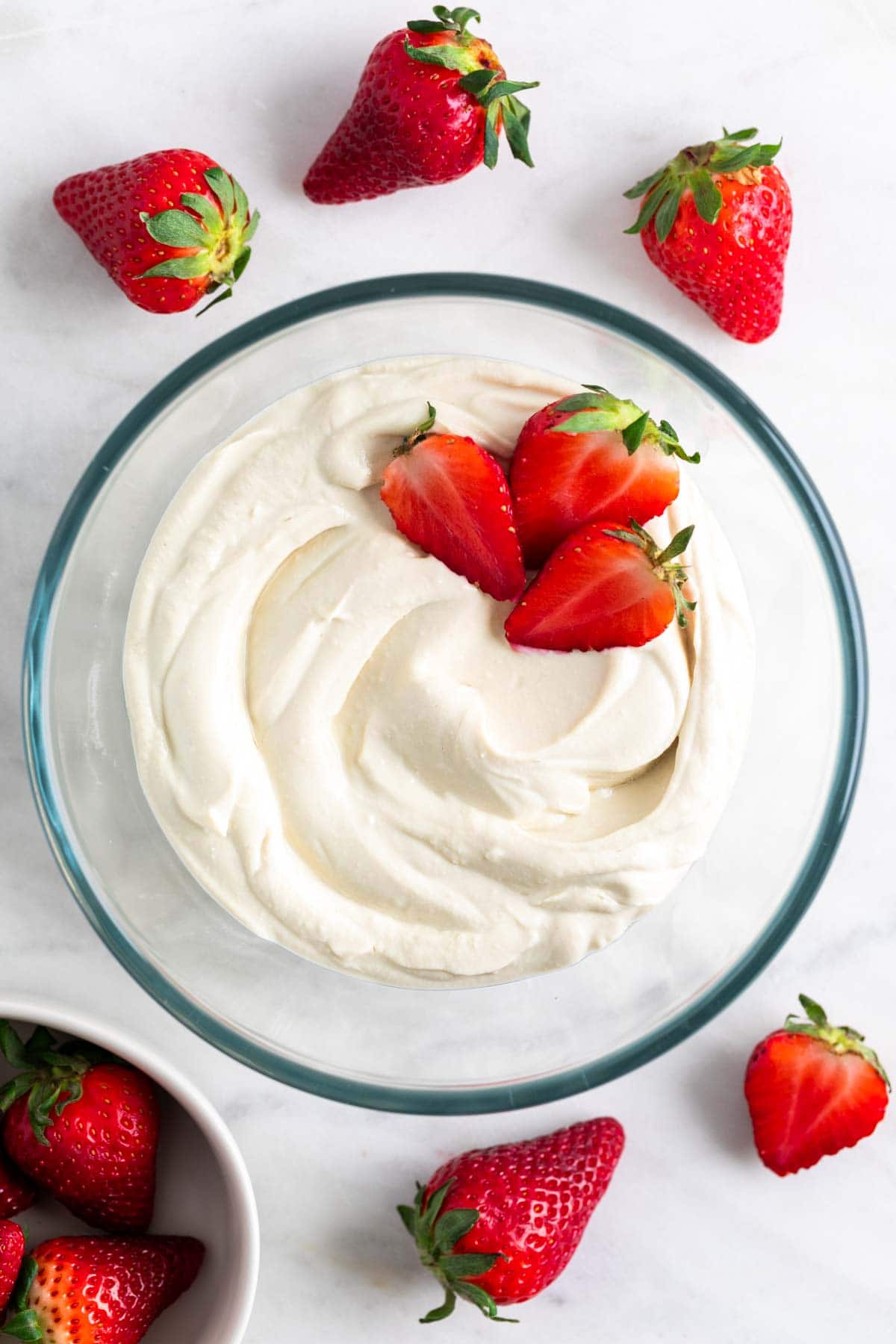 Vegan mascarpone cheese in a glass bowl surrounded by fresh strawberries.