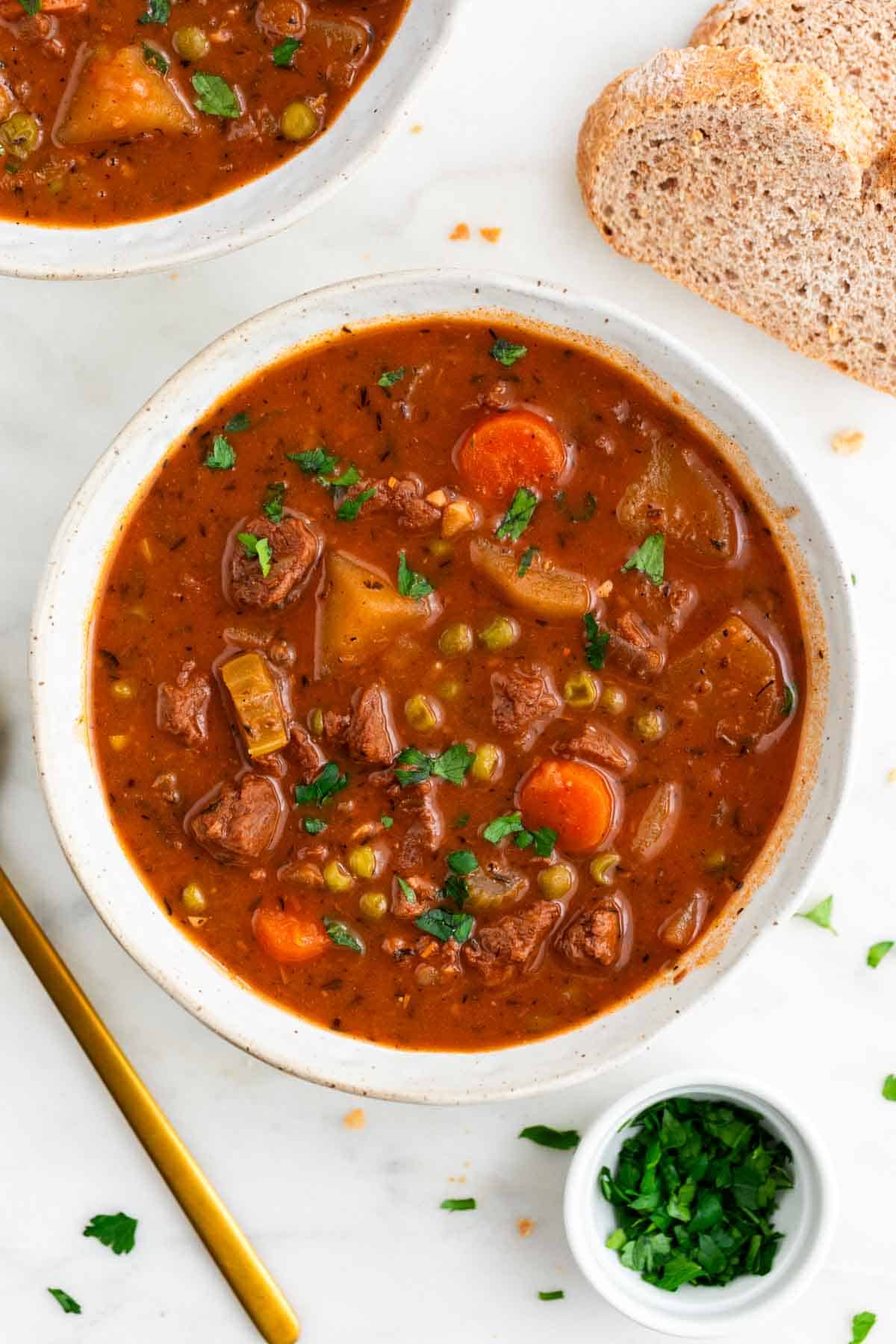 Vegan beef stew served in a bowl with bread and parsley around it.