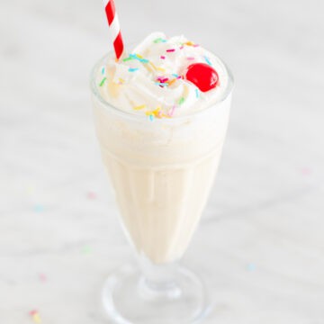 Vegan ice cream in a glass topped with various toppings and a straw.