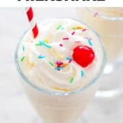 Vegan milkshake in a glass, topped with whipped cream, sprinkles, a cherry, and a straw.