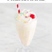 Glass of vegan milkshake topped with vegan whipped cream, colorful sprinkles, and a cherry.