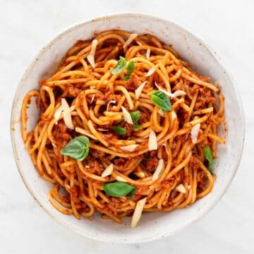 Vegan spaghetti in a bowl with basil leaves and shredded vegan cheese on top.