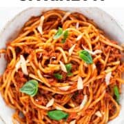 A bowl of vegan spaghetti with vegan cheese and basil on top.
