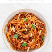Vegan spaghetti in a bowl garnished with basil and vegan cheese.