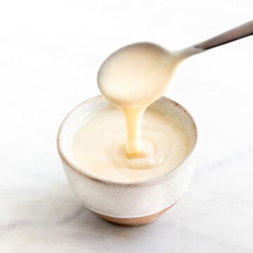 Spoon dipping into bowl of vegan sweetened condensed milk.
