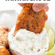 Hand dips vegan fish into vegan tartar sauce.