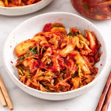 Vegan kimchi in two shallow dishes and in a jar.