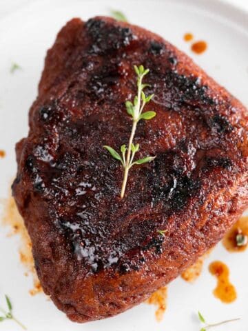Vegan steak presented on a white plate, garnished with fresh thyme.