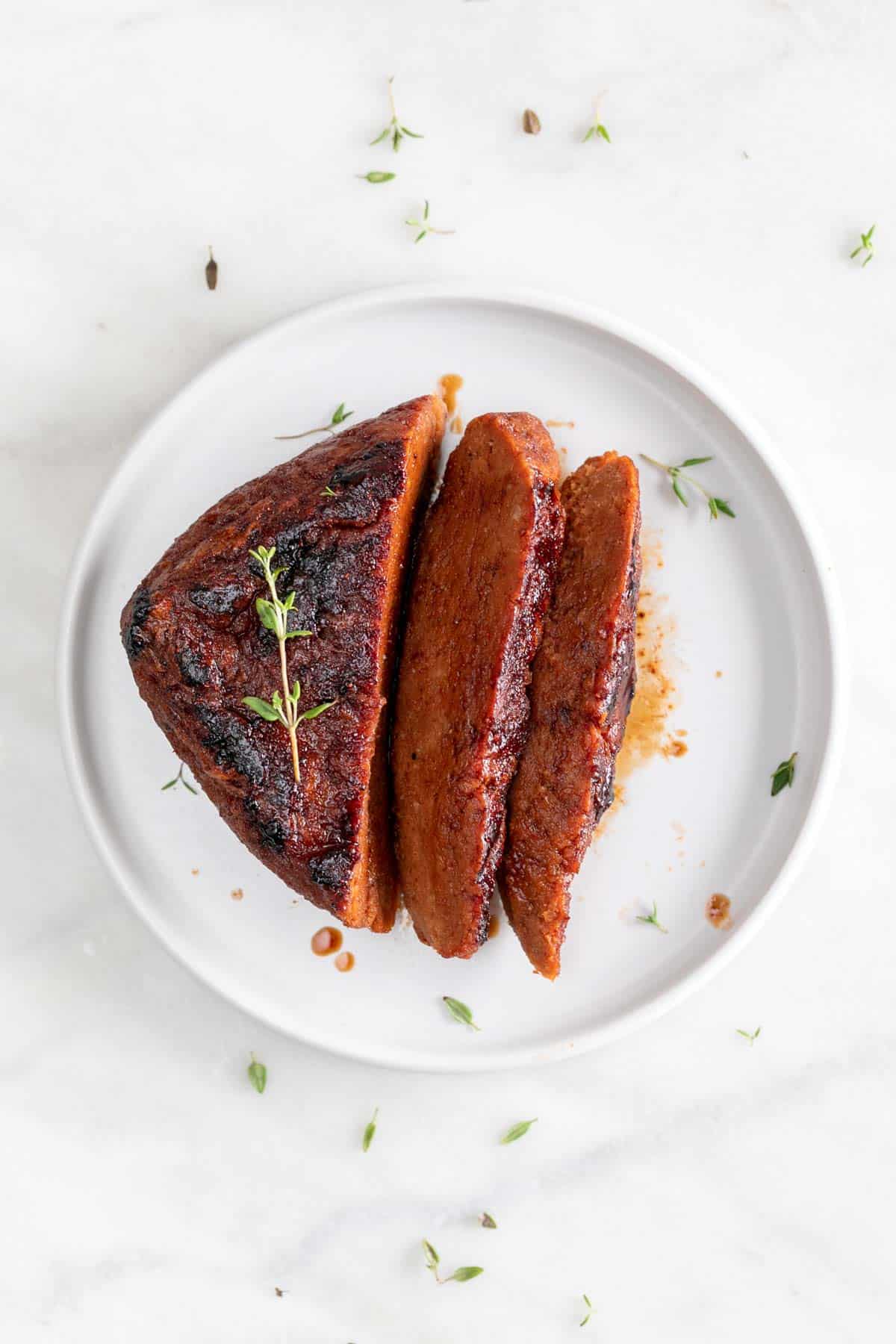 Vegan steak sliced on a white plate with fresh thyme on top.