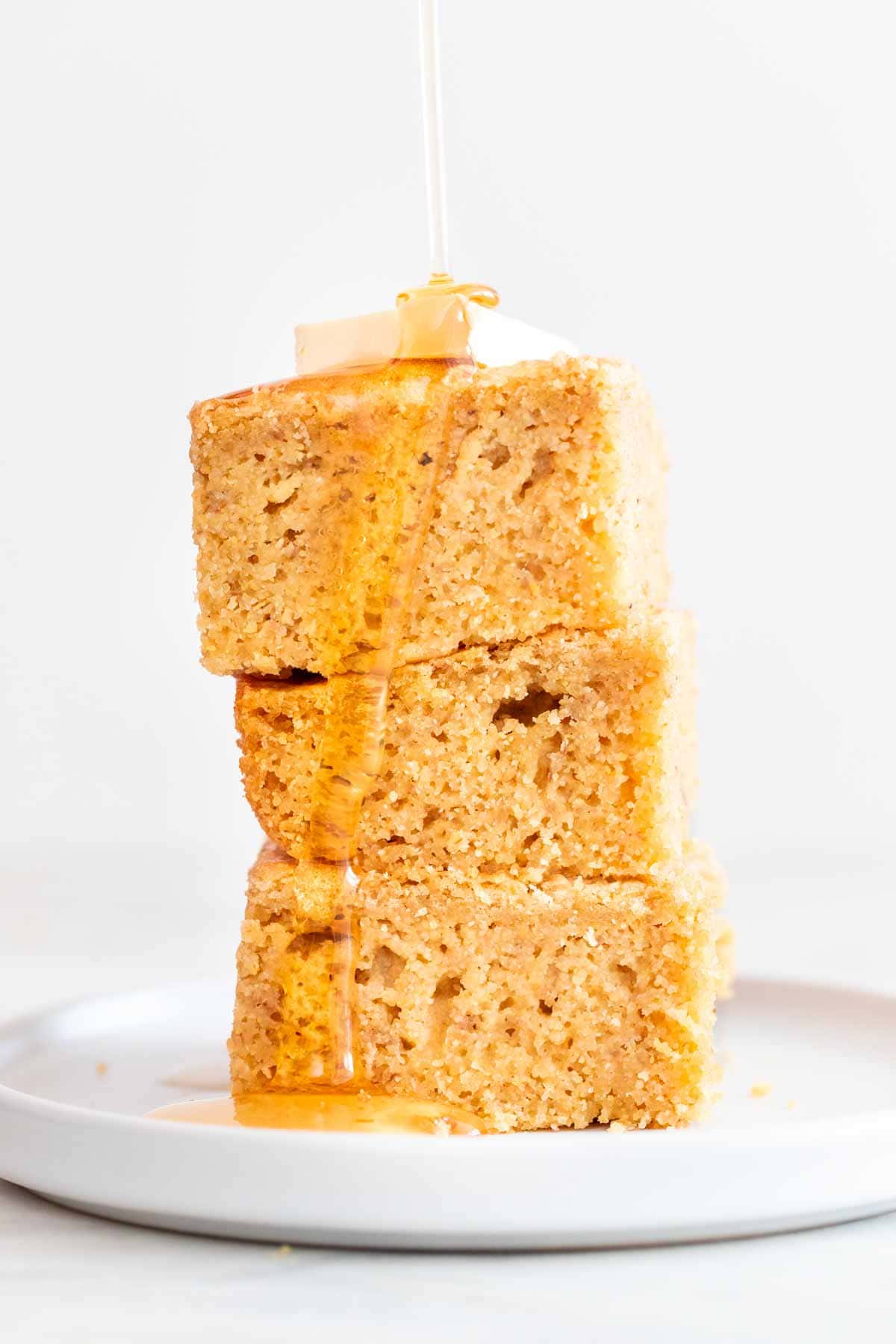 Vegan cornbread squares stacked up topped with some vegan butter and agave syrup.