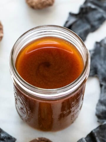 Jar of vegan fish sauce with seaweed and dried mushrooms in the background.