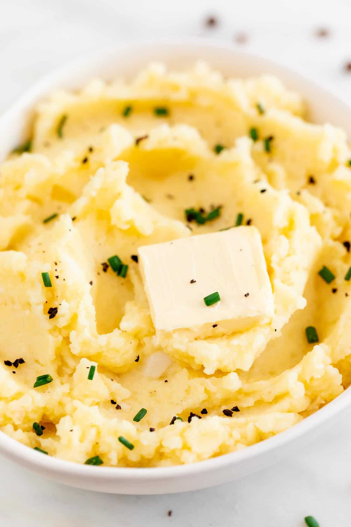 Bowl with vegan mashed potatoes topped with vegan butter and garnished with chives and pepper.