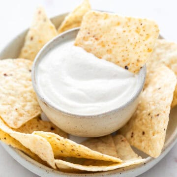 Vegan sour cream surrounded by tortilla chips with one chip dipped inside.