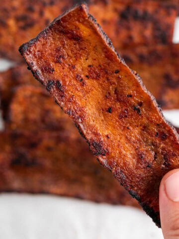 Tofu bacon slices on a white background with a finger picking up a slice.