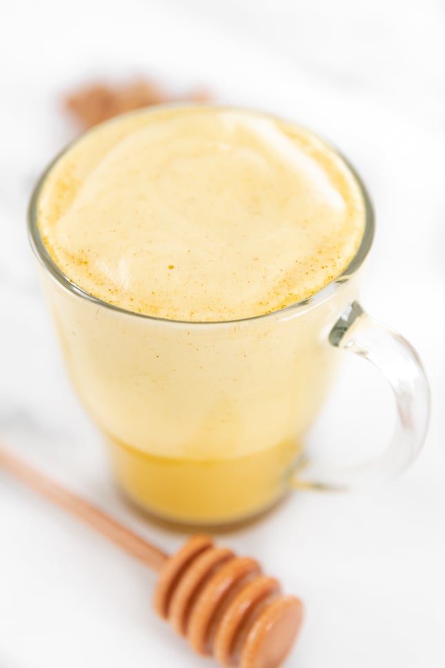 Photo of a glass cup of turmeric latte with a honey spoon