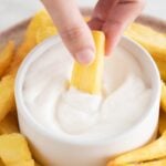 Photo of a dish with French fries and a small bowl with vegan aioli and a hand dipping a fry into the sauce with a heading.