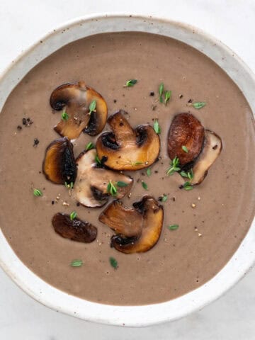 Bowl of creamy mushroom soup topped with black pepper, fresh thyme, and sautéed mushrooms.