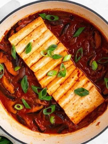 Vegan kimchi stew in a large pot with scallions on top, and a bowl of extra scallions on the side.