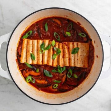Vegan kimchi stew in a large pot with scallions on top.