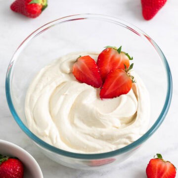Vegan mascarpone in a glass bowl with fresh strawberries and more strawberries around it.