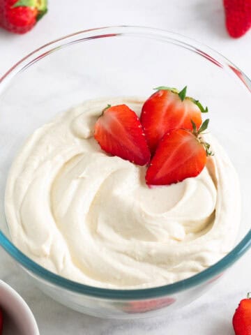 Vegan mascarpone in a glass bowl with fresh strawberries and more strawberries around it.
