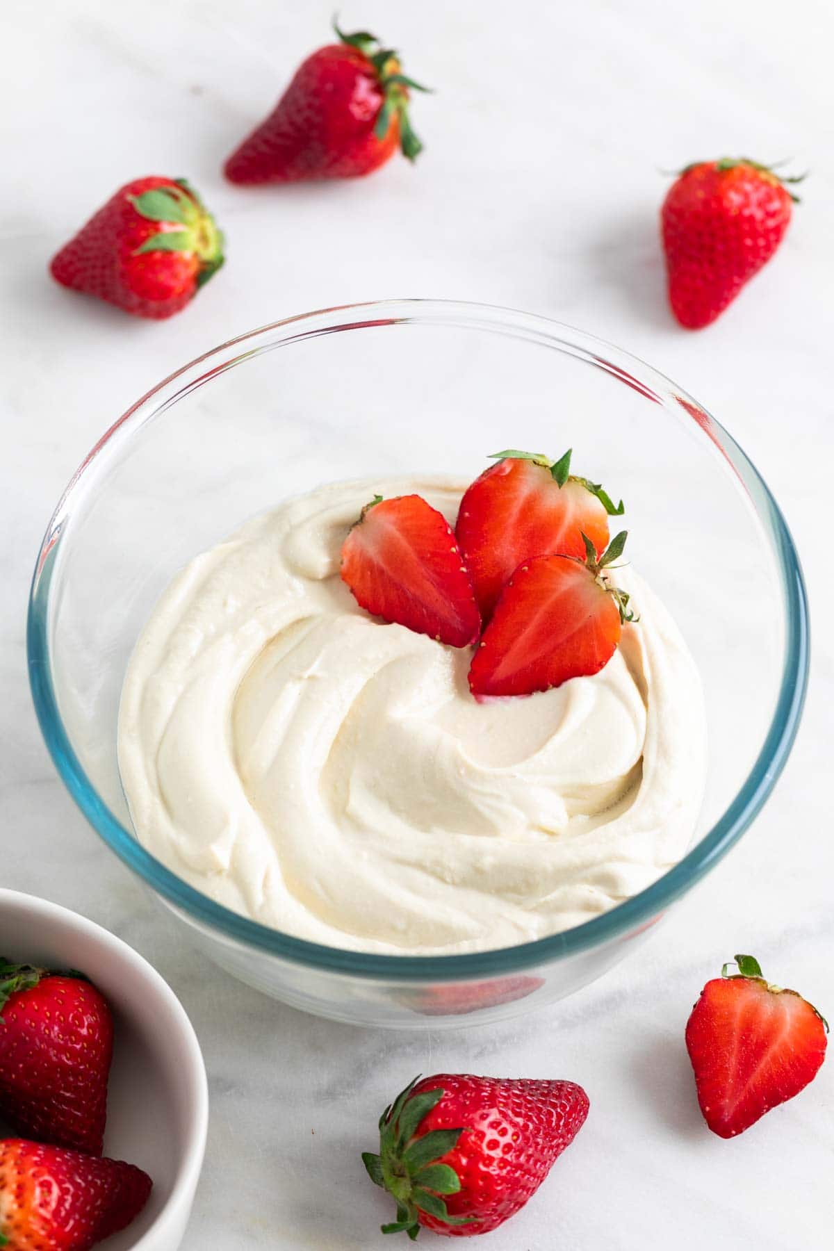 Vegan mascarpone in a glass bowl with fresh strawberries and more strawberries around it.
