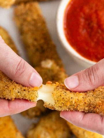 Two hands breaking a vegan mozzarella stick in half.