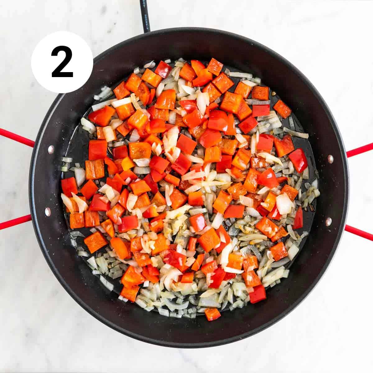 Onion and red bell pepper sautéed in a paella pan.