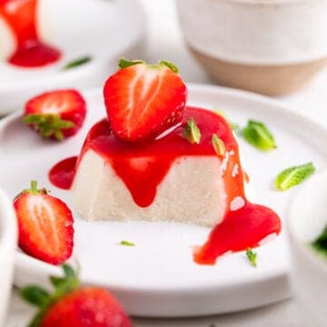 Vegan panna cotta on a plate, cut to reveal the inside, topped with strawberry coulis, a strawberry, and mint leaves.