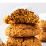Three vegan pumpkin cookies in a stack, with the top one frosted and a bite missing.