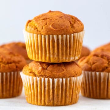 Stacked vegan pumpkin muffins with more muffins in the background.