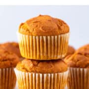 Vegan pumpkin muffins arranged in a stack, surrounded by additional muffins.