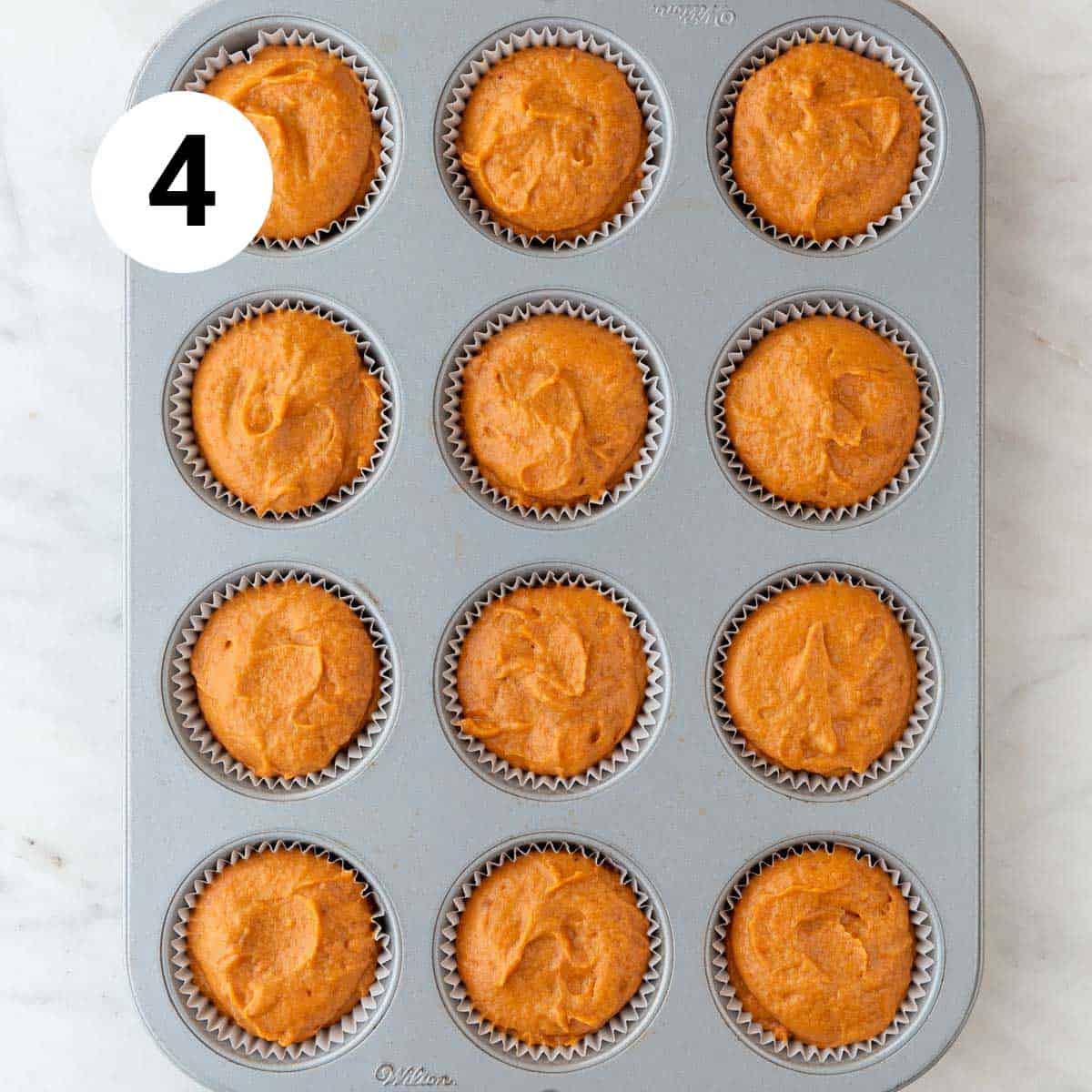 Muffin pan with liners filled with vegan pumpkin muffin batter.