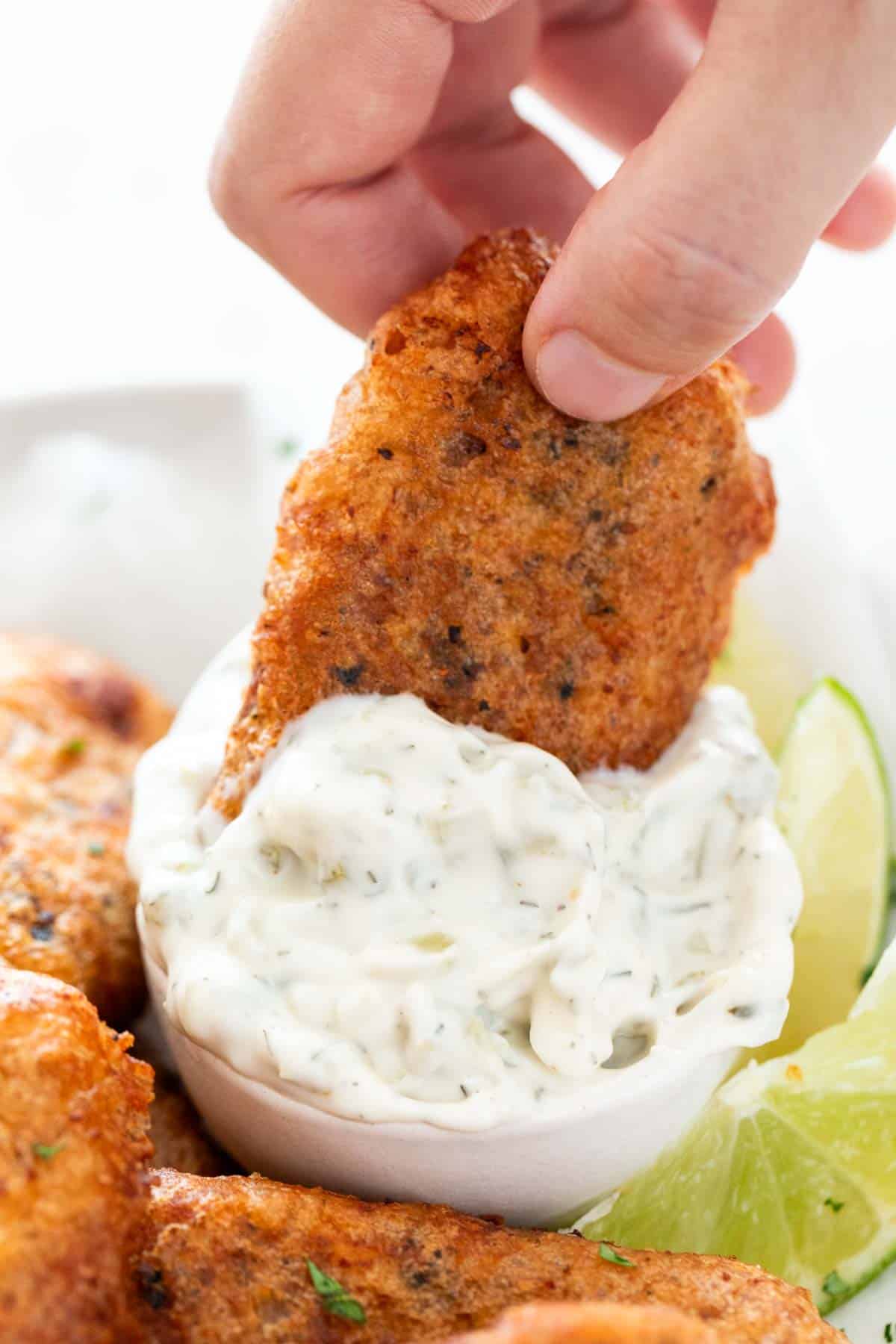 Hand dipping vegan fish into vegan tartar sauce bowl.