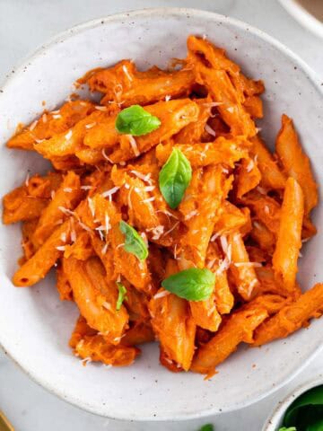 Vegan penne alla vodka in a bowl, garnished with basil and vegan parmesan cheese.