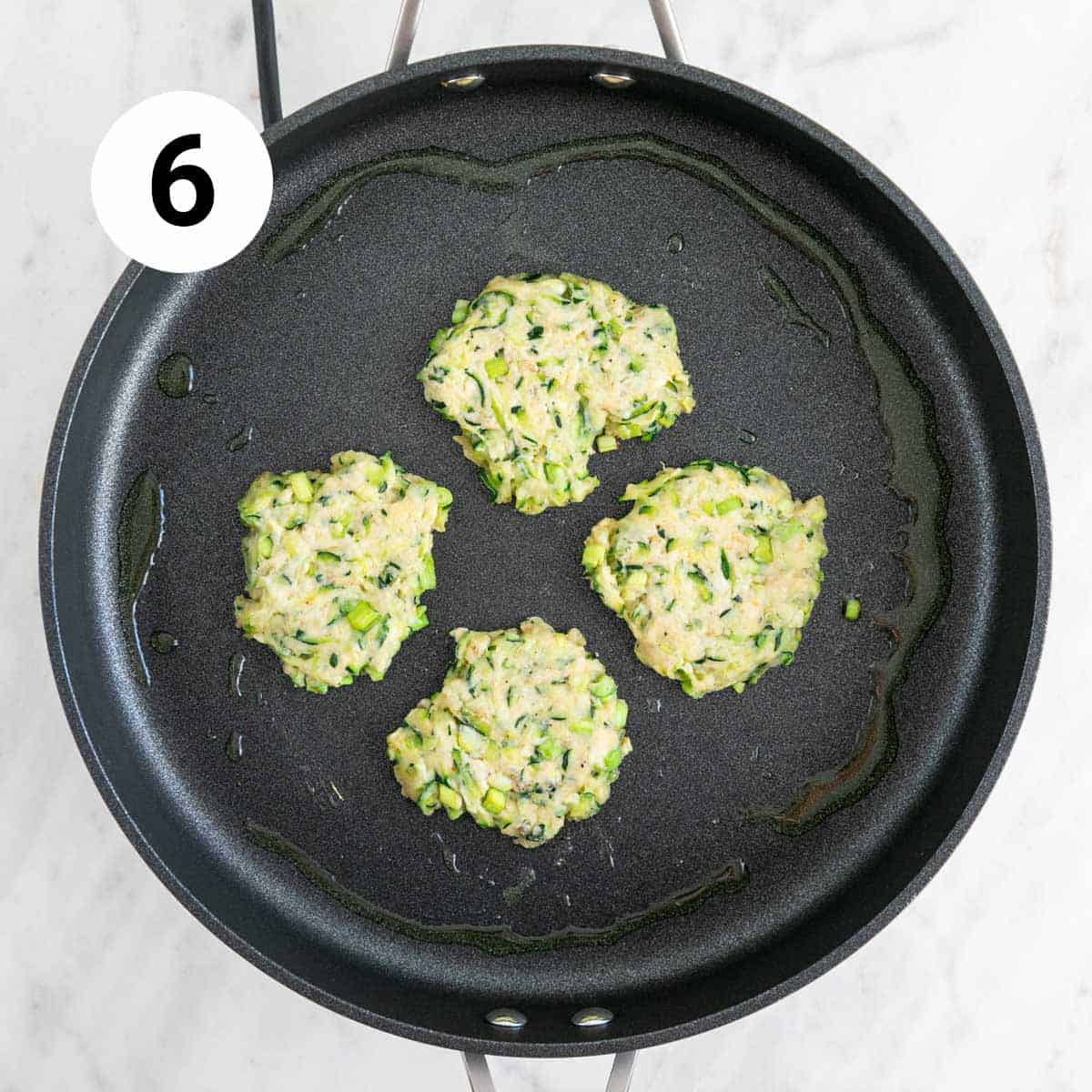 Vegan zucchini fritters cooking in a frying pan.