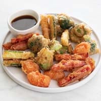 A small photo of vegetable tempura in a plate with a small bowl with soy sauce