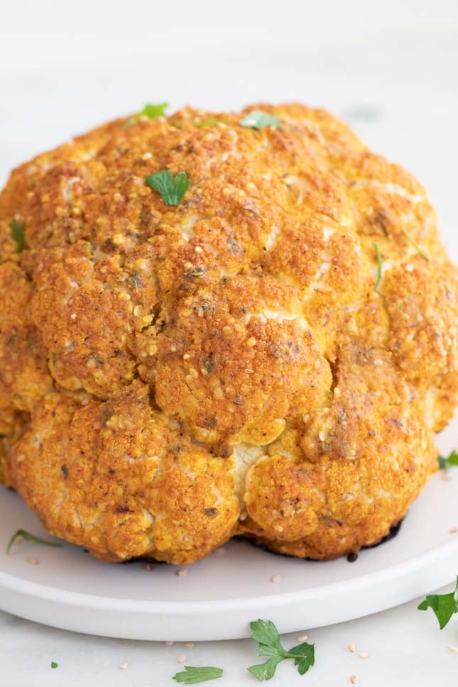 A side shot of a roasted cauliflower onto a dish with some parsley on top